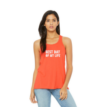medium-skinned person with long brown hair wearing an orange tank top with best day of my life written across in white block lettering.